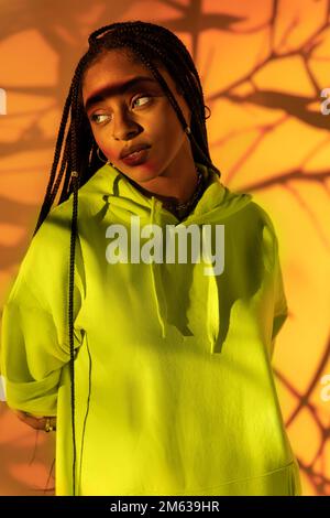 Young African American female with Afro braids standing against bright orange light looking away Stock Photo