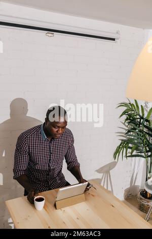 Thoughtful Black Man with a Digital Tablet on a Wooden Table Stock Photo