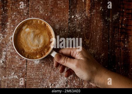 Top view of crop anonymous person with cup of aromatic coffee with foam on wooden table Stock Photo