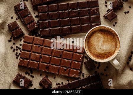 From above cup of hot aromatic coffee placed on wooden table near set of chocolate bars with Stock Photo