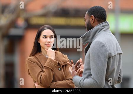 Suspicious woman listening a man talking in the street in winter Stock Photo