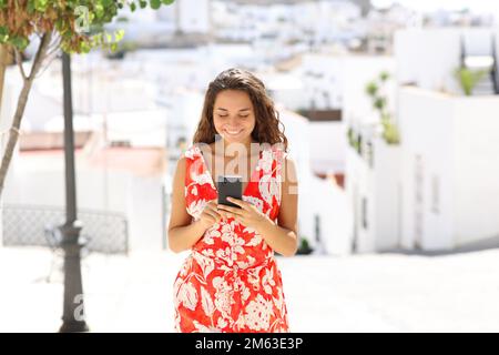 Front view portrait of a happy tourist using smart phone walking in a white spanish town Stock Photo