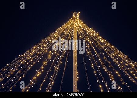 Yellow lights garlands outdoor hanging wires from pillar at night blue sky background, magic holiday atmosphere. Festive Christmas garlands with lumin Stock Photo