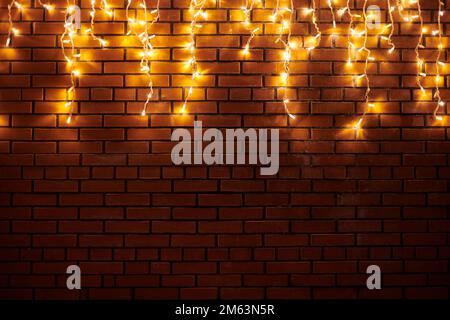 Yellow lights garlands hanging from red brick wall at evening, beautiful christmas house decoration with magic holiday atmosphere. Festive Christmas g Stock Photo
