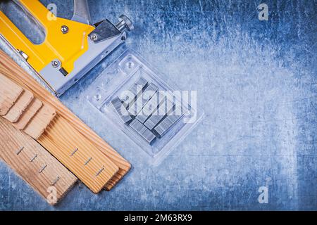 Yellow construction stapler metal staples wooden building board on metallic background. Stock Photo