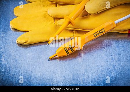 Yellow electrical tester safety gloves on metallic background. Stock Photo