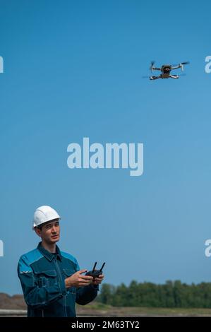 A man in a helmet and overalls controls a drone at a construction site. The builder carries out technical oversight. Stock Photo