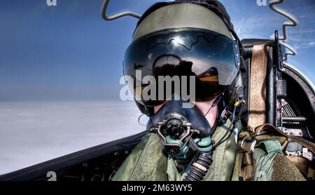 Fighter pilot in a jet flying high in the sky with visor, helmet and oxygen mask against a blue sky. Cool selfie. Stock Photo