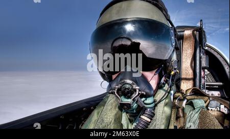 Pilot in the cockpit in an ejector seat wearing helmet, visor and oxygen mask flying high above the clouds Top Gun style fighter pilot black visor Stock Photo