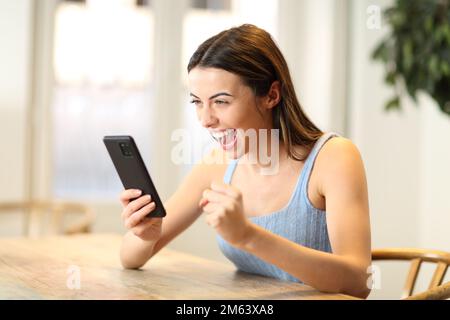 Excited woman checking smart phone content at home Stock Photo