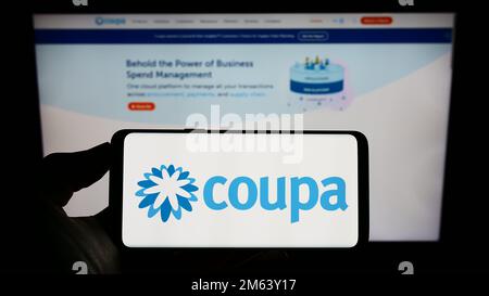 Person holding cellphone with logo of spend management company Coupa Software Inc. on screen in front of business webpage. Focus on phone display. Stock Photo