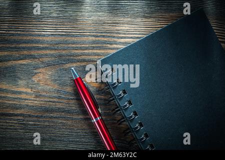 Black spiral notebook biro pen on vintage wooden board. Stock Photo