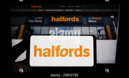 Person holding smartphone with logo of British retail company Halfords Group plc on screen in front of website. Focus on phone display. Stock Photo