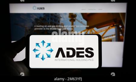 Person holding smartphone with logo of Egyptian company ADES International Holding on screen in front of website. Focus on phone display. Stock Photo