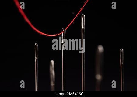 Red thread passing through needles on a black background. Stock Photo