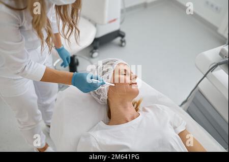 Cosmetologist drawing with white pencil on patient face Stock Photo