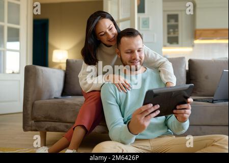 Happy young family couple using mobile tablet at home together Stock Photo
