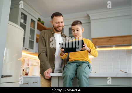 Father with son using digital tablet together at home kitchen Stock Photo