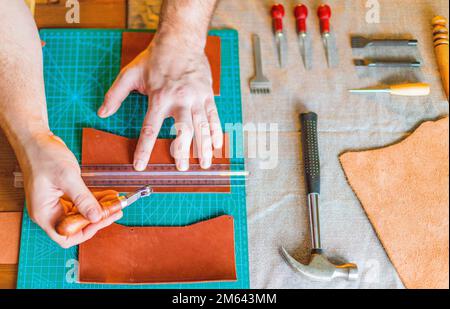Working process of the leather bag for money or messenger in the leather workshop by master craftsman hands on the table background. Color tone image Stock Photo