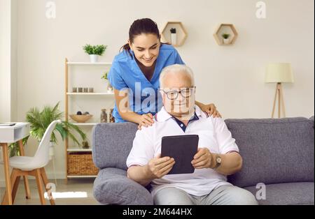 Nurse or caregiver helping happy retired senior man to use modern tablet computer Stock Photo