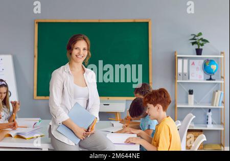 Portrait of beautiful smiling female teacher in school classroom on background of schoolchildren. Stock Photo