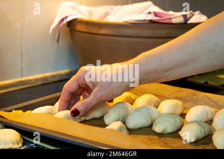 A woman's hand puts small raw pies in a pan. Meat pies are traditional Latvian holiday dishes Stock Photo