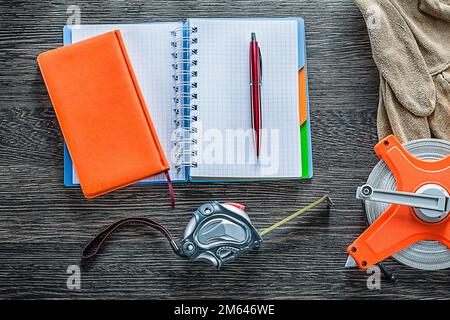 Rolled tape measures safety gloves notebooks pen on wooden board. Stock Photo