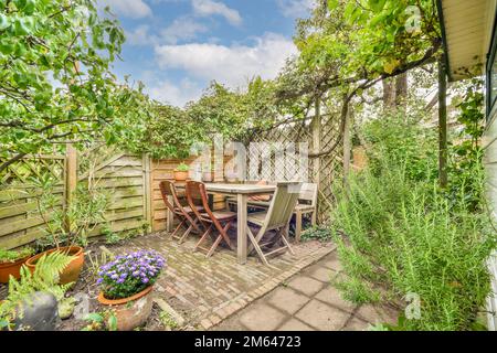 an outdoor patio with table, chairs and potted plants in the background is a wooden fenced garden area Stock Photo