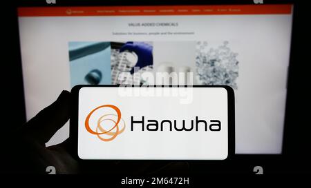 Person holding smartphone with logo of South Korean company Hanwha Group on screen in front of website. Focus on phone display. Stock Photo