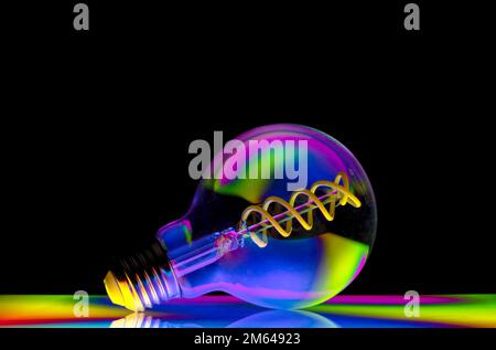Colourful patterns reflect within a clear glass round shaped lightbulb, photographed against a black background Stock Photo