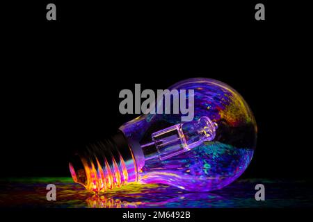Colourful patterns reflect within a clear glass round shaped lightbulb, photographed against a black background Stock Photo