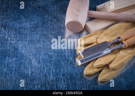 Wooden mallet studs firmer chisels and protective gloves on scratched metallic surface construction concept. Stock Photo