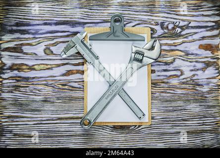 Vernier caliper adjustable wrench clipboard on wooden board. Stock Photo