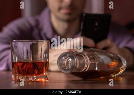A businessman drinks alcohol and looks at information through his smartphone. Drink alcohol in the home. Alcoholic Stock Photo