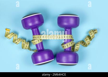 Dumbbells and measuring tape on blue background. Stock Photo