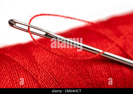 Eye of the needle with red polyester thread. Spool of red polyester sewing thread in the background. Selective focus. Bokeh. Stock Photo