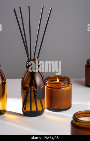 Aroma diffuser with natural essential oil in brown glass bottle, soy wax candle with fire in Amber jar on white gray background. Concept mental health Stock Photo