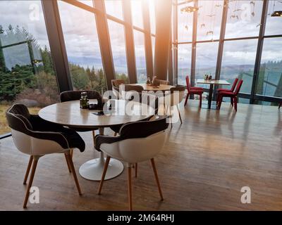 Tables and chairs set in modern cafe minimalistic interior design with big window and hanging ceiling lamps Stock Photo