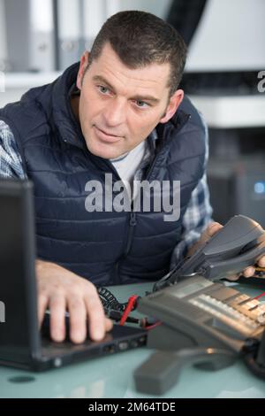 technician looking at laptop while repairing a telephone Stock Photo