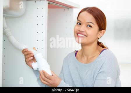 woman fitting water trap under kitchen sink Stock Photo