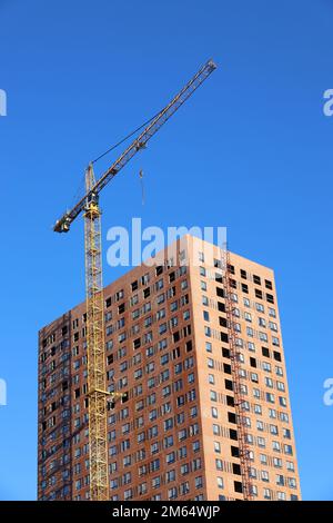 Tower crane and unfinished building on background of blue sky, vertical shot. Housing construction, apartment blocks in city Stock Photo
