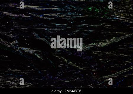 Black color plastic wrap background. Dark crumpled wrinkled plastic cellophane. Reflecting blue light and shadow on creases and folds in plastic Stock Photo