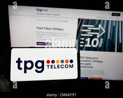 Person holding smartphone with logo of Australian company TPG Telecom Limited on screen in front of website. Focus on phone display. Stock Photo