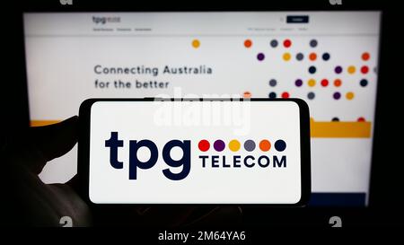 Person holding cellphone with logo of Australian company TPG Telecom Limited on screen in front of business webpage. Focus on phone display. Stock Photo