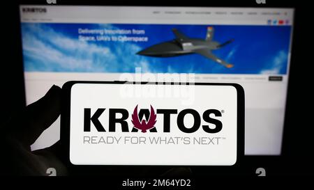 Person holding smartphone with logo of company Kratos Defense Security Solutions Inc. on screen in front of website. Focus on phone display. Stock Photo