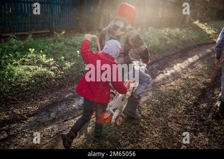 A girl pushes a bicycle with her older brother. Children of immigrants have fun in the village. A remote village without roads. Ukrainian children mov Stock Photo