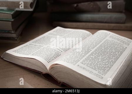 Image of an old book open by a random page on a table with many other old books of different colors Stock Photo