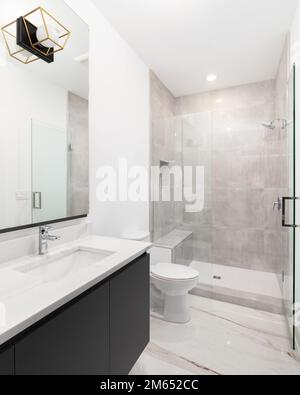 A bathroom with a dark grey floating cabinet, white marble countertop, and a brown marble tiled shower. Stock Photo