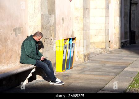Man sitting on bench checks notifications on smartphone Stock Photo