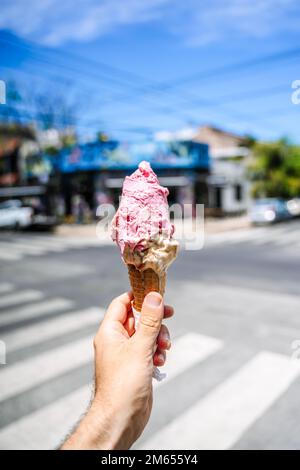 Ice cream in hand. Waffle cone with ice cream on the background of the street in the summer on a hot day. Street food, sweets, desserts concept. High quality photo Stock Photo